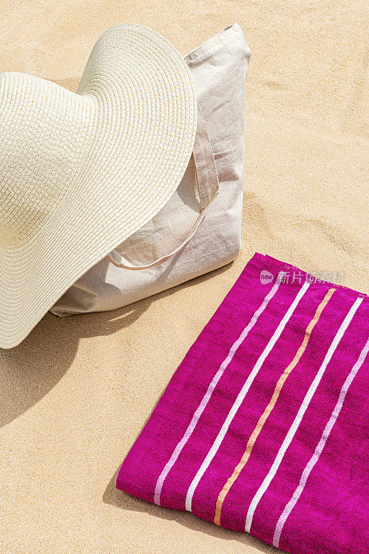 草帽放在帆布袋上，毛巾放在沙滩上