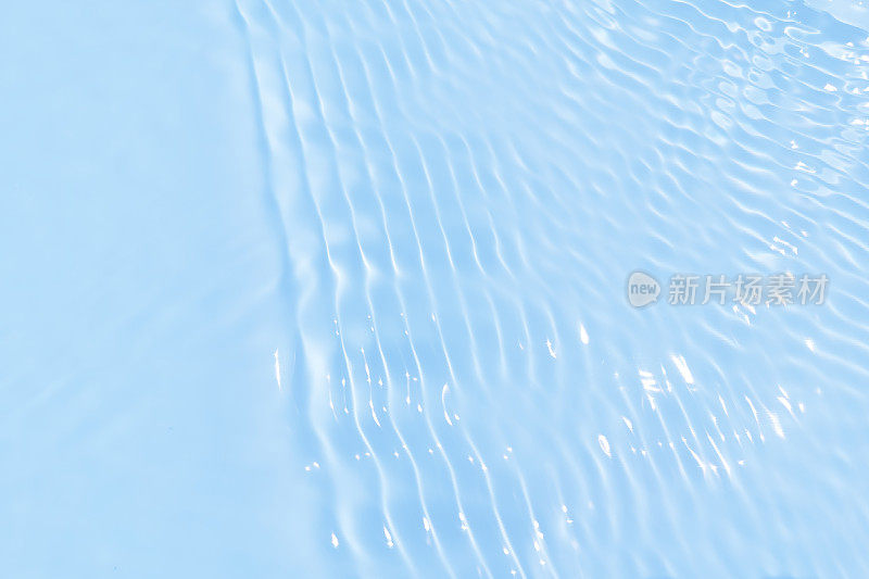 离焦模糊透明的蓝色清澈平静的水面纹理带有水花、气泡。粼粼碧水涟漪背景。游泳池的水面。蓝色的泡泡水闪闪发光。