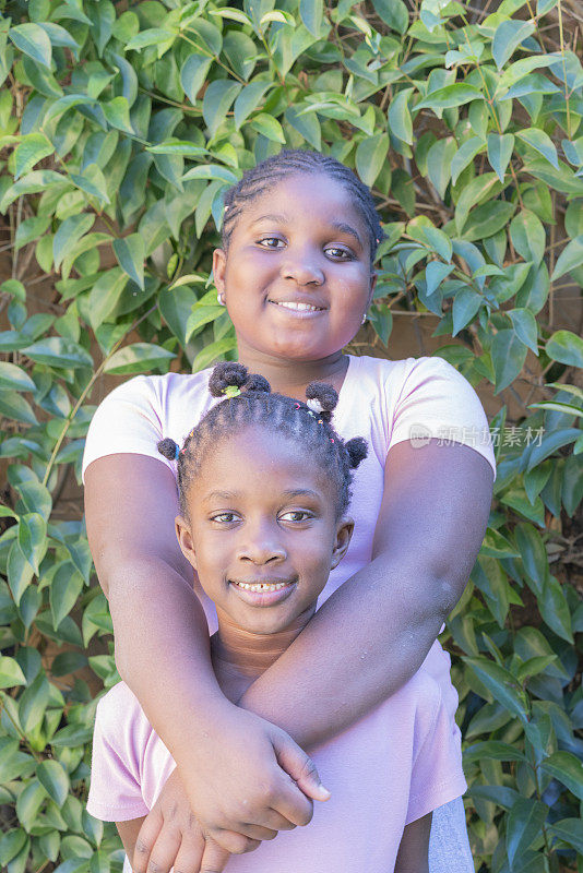 幸福的美国黑人小姐妹在户外花园一起微笑的肖像