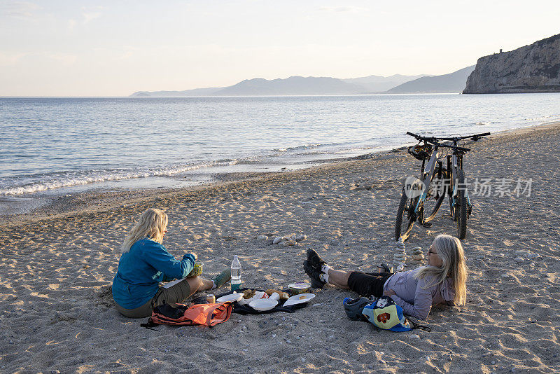 高级女自行车手在海滩上野餐
