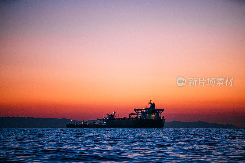 日落时，一艘大型空货船在加利福尼亚州亨廷顿海滩的太平洋上的剪影，背景是卡塔利娜岛的景色