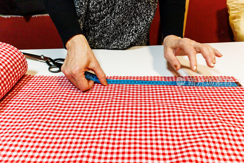一个女裁缝正在车间里用剪刀和尺子准备布料。