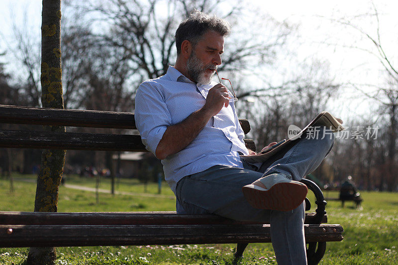 一个成熟的男人坐在长凳上看报纸
