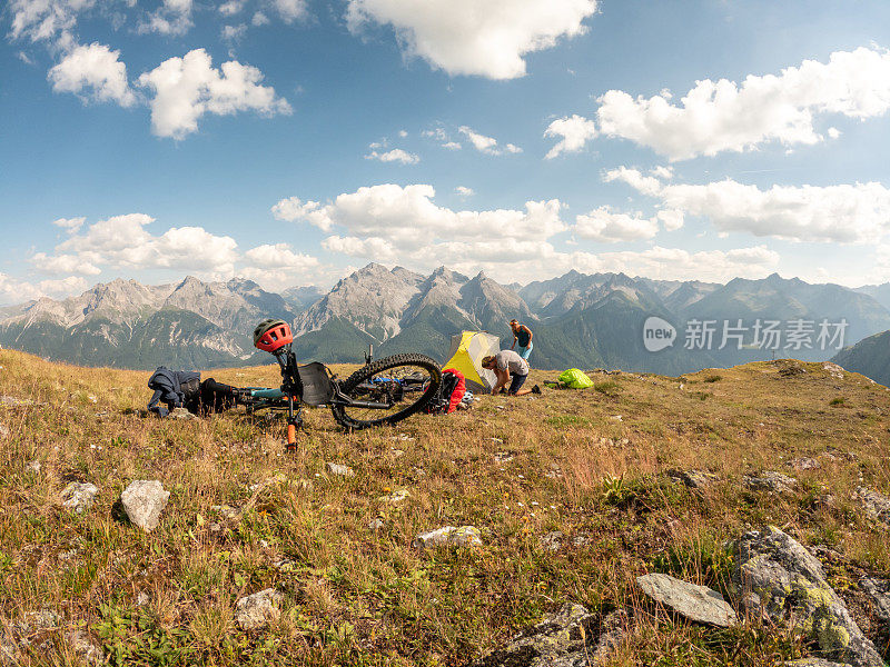 一对夫妇在瑞士阿尔卑斯山骑自行车，日落时分在山顶搭起帐篷