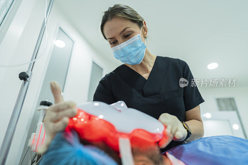 美容师在给病人戴上红光面具的同时进行美容手术