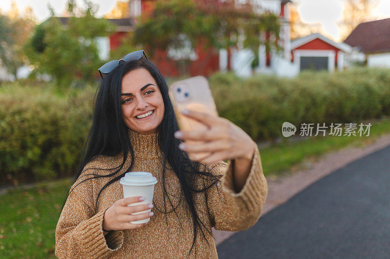 美丽的年轻女子拿着咖啡杯在户外自拍