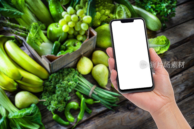 手持空白屏幕手机对散焦绿色水果和蔬菜的背景