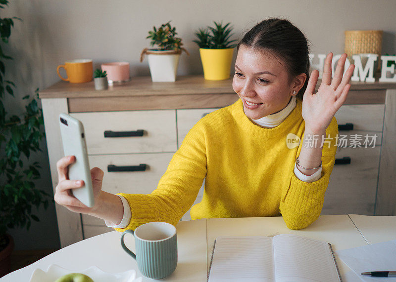 一个年轻的女孩正在进行视频通话。他用智能手机挥手。