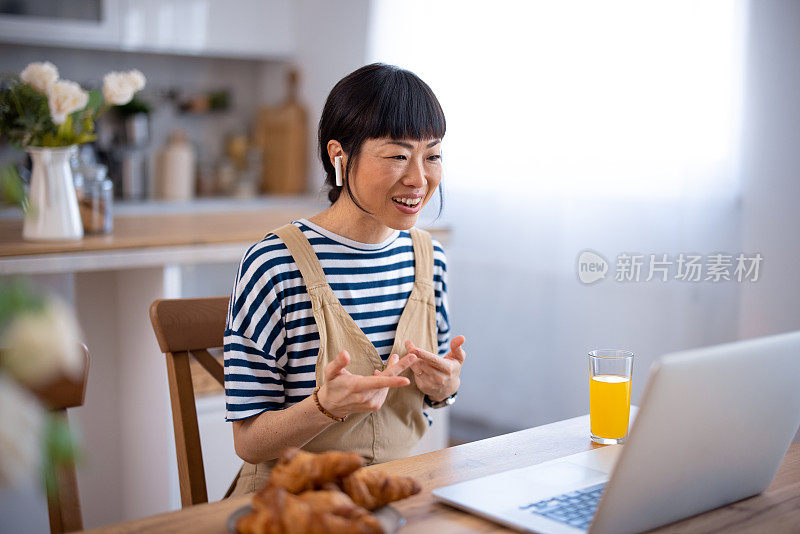 一个亚洲女人一边用笔记本电脑打字一边吃早餐