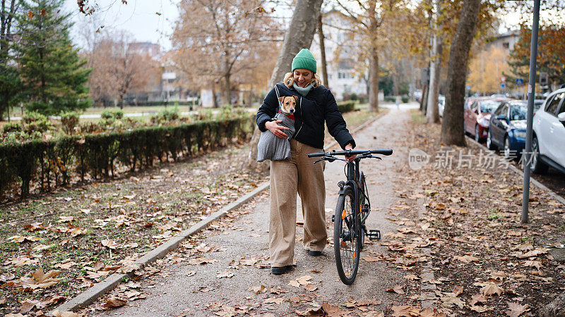 穿着随意的女人推着她的自行车，把她的狗放在包里