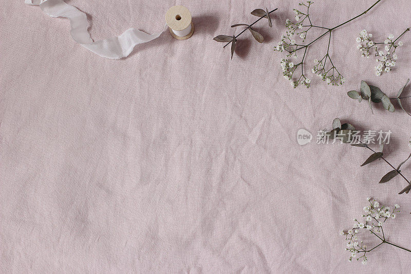 鲜花婚礼，生日桌构成。在粉红色亚麻布桌布的背景上，槐树、桉树叶和绸带。平躺，俯视图。复制空间，没有人。