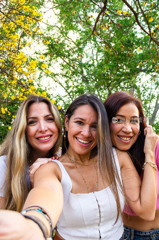 夏日黄金时段，三位漂亮的成年女性朋友在户外公园自拍。友谊与幸福概念