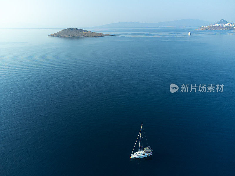 从无人机上看，一艘游艇在开阔的海面上挂着白色的帆。美丽的豪华游艇，帆船在蓝色的波浪上航行。从无人驾驶飞机上看到的蓝色水面上的游艇。