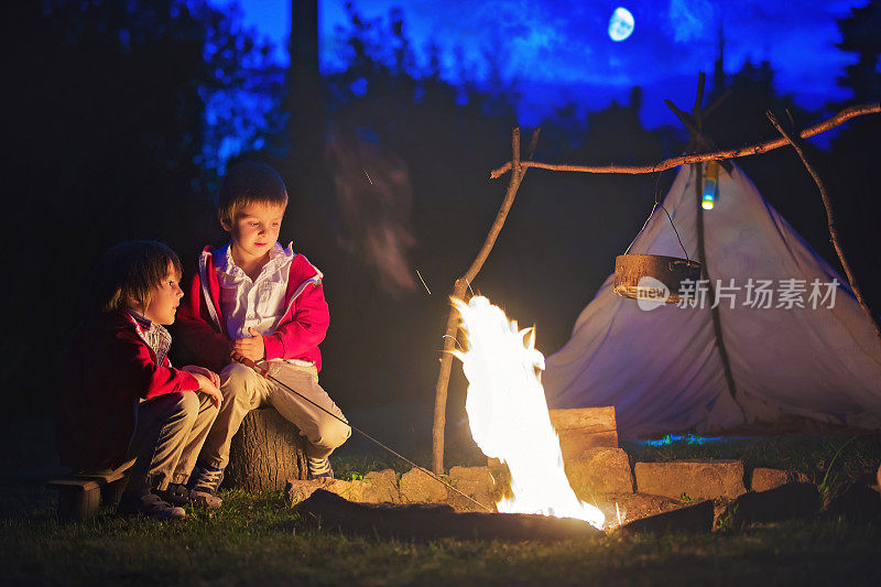 两个可爱的男孩，太阳落山后围坐在篝火旁