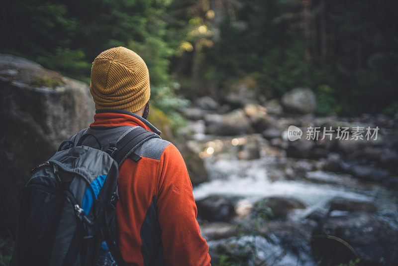 一个背包的旅行者看着山间的河流