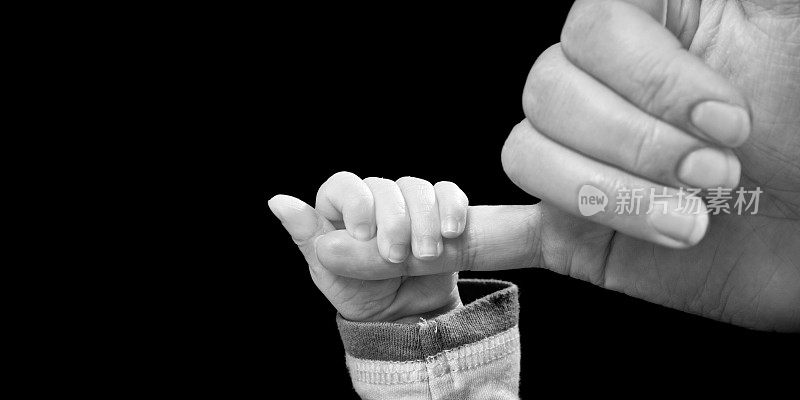 婴儿抱着妈妈的手指在黑色的背景