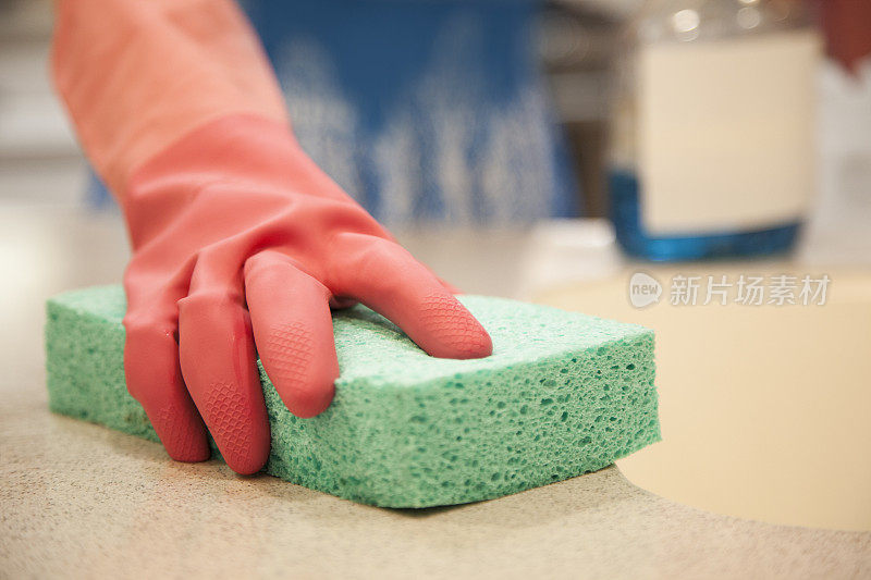 一个妇女正在用海绵和清洁剂清洁厨房。