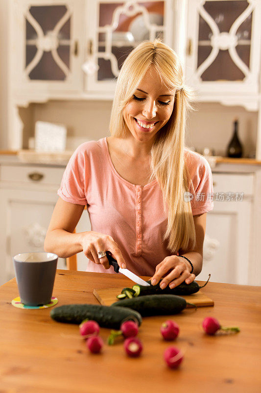 微笑的女人在厨房切黄瓜。