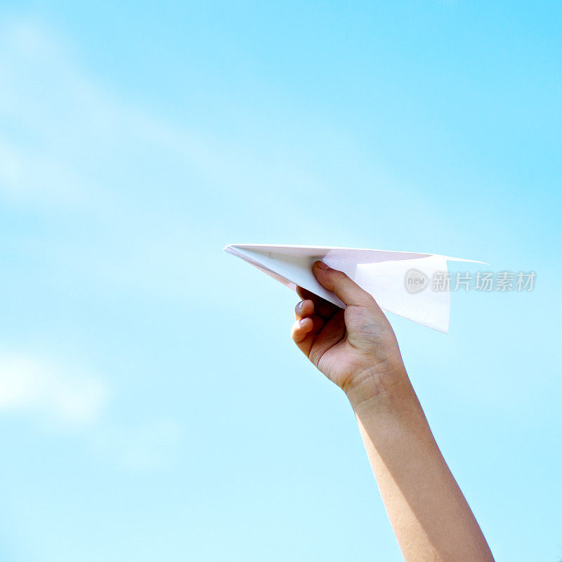 在天空的背景下，男孩手拿着纸飞机