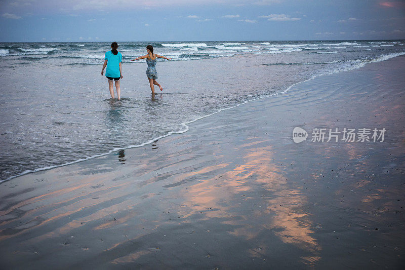 两个少年在粉红色的夕阳下在海里奔跑