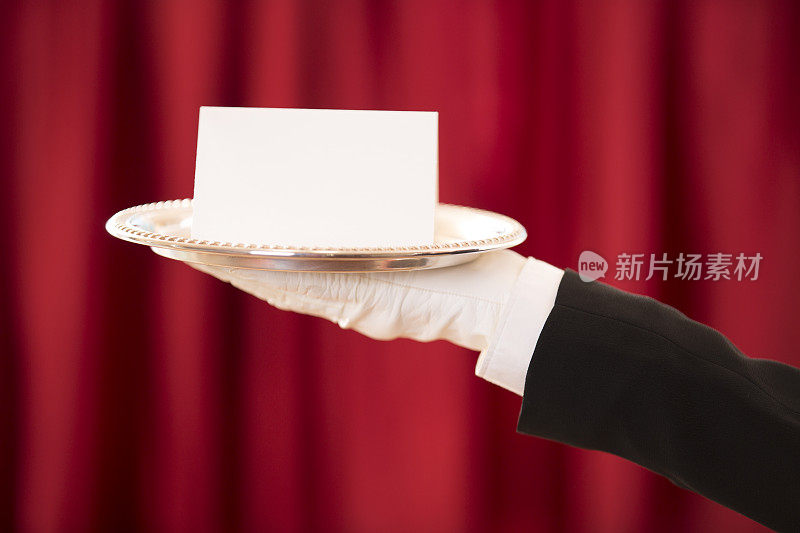巴特勒拿着白色的空白卡片放在银盘子里。红色的窗帘。
