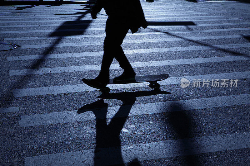 孤独的青年滑着滑板走在城市街道蓝色夜晚的阴影