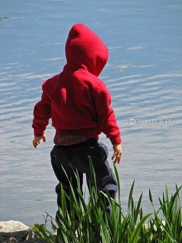 小孩子站在水附近在红色兜帽运动衫