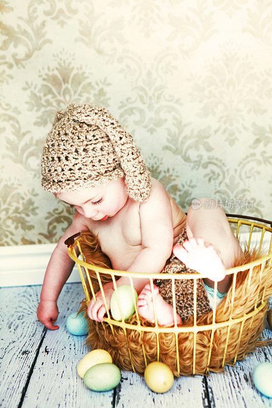 戴着兔耳朵的婴儿坐在古董蛋筐里