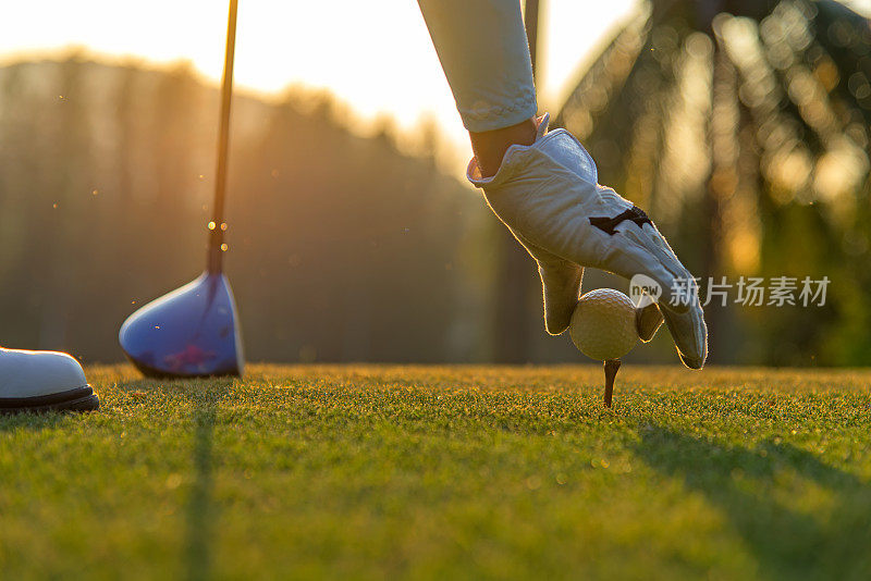在傍晚和日落时分，亚洲妇女在高尔夫球场用球杆把高尔夫球放在球座上，这是一项有益于健康的运动。生活方式的概念