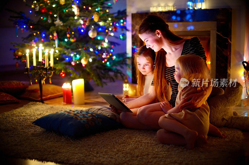 母亲和女儿在圣诞节壁炉旁使用平板电脑