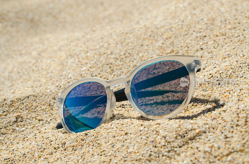 在海滩上戴墨镜。多色时尚的模型与透明框架和蓝色镜头。假期的概念。