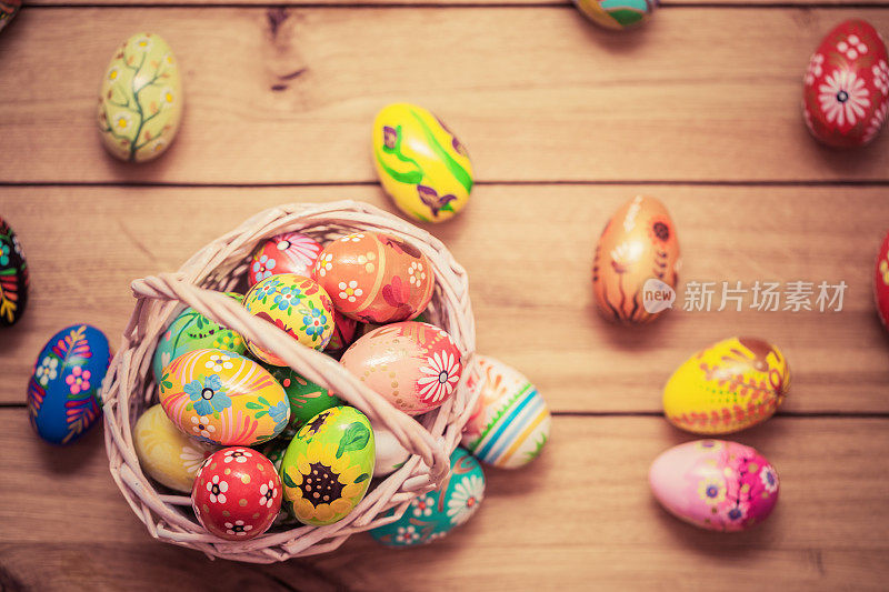 彩色的手绘复活节彩蛋在篮子和木头上。手工制作的装饰