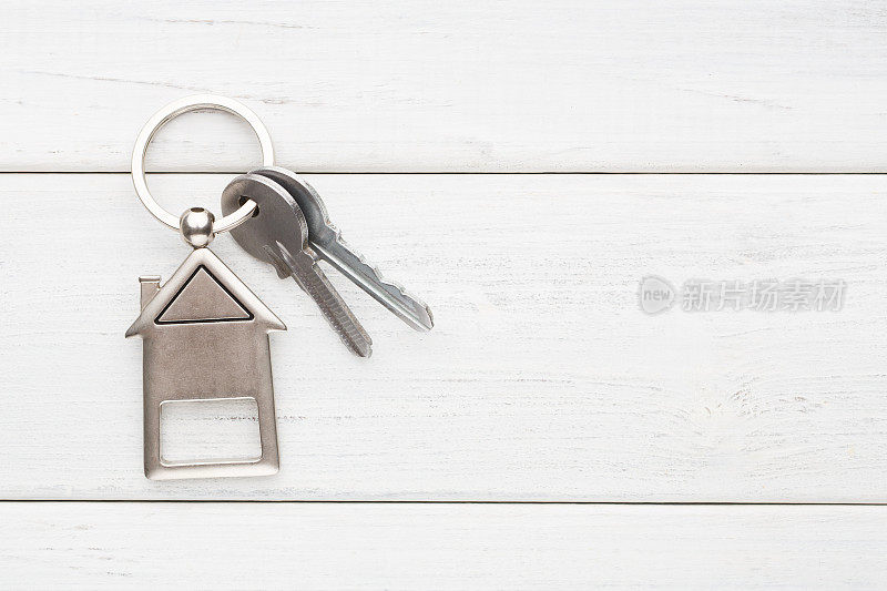 一串钥匙和房子形状的钥匙链在白色木头上