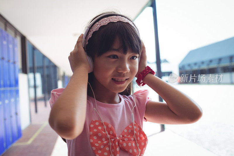 走廊里微笑的女孩戴着耳机听音乐