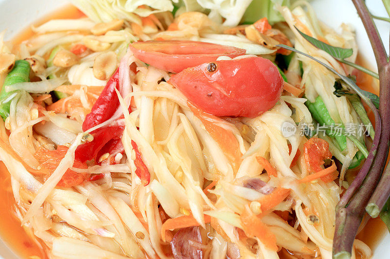 木瓜沙拉配胡萝卜，扁豆，番茄，虾米，辣椒，白盘子，木背景。泰国风格的食物。