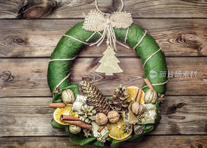 圣诞花环挂在木门上，用干香料和水果装饰在棕色的乡村木头上