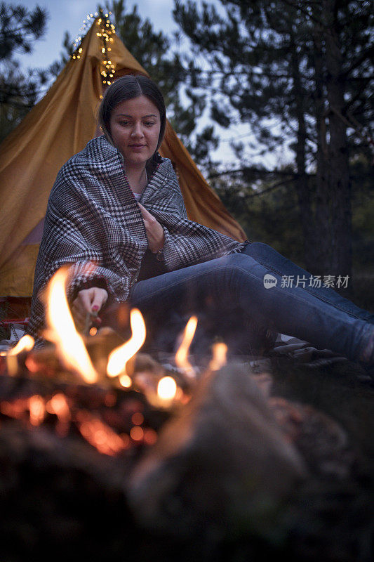 一个女旅行者在一个帐篷的背景下靠火休息