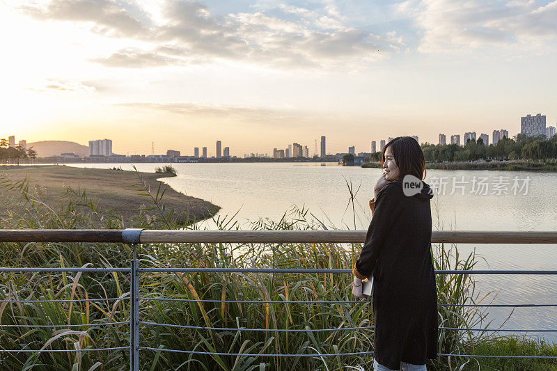 年轻女子在公园人行桥上欣赏美丽的日落风景