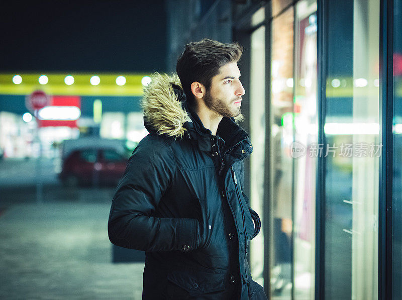 年轻人走在晚上，看着城市商店的橱窗