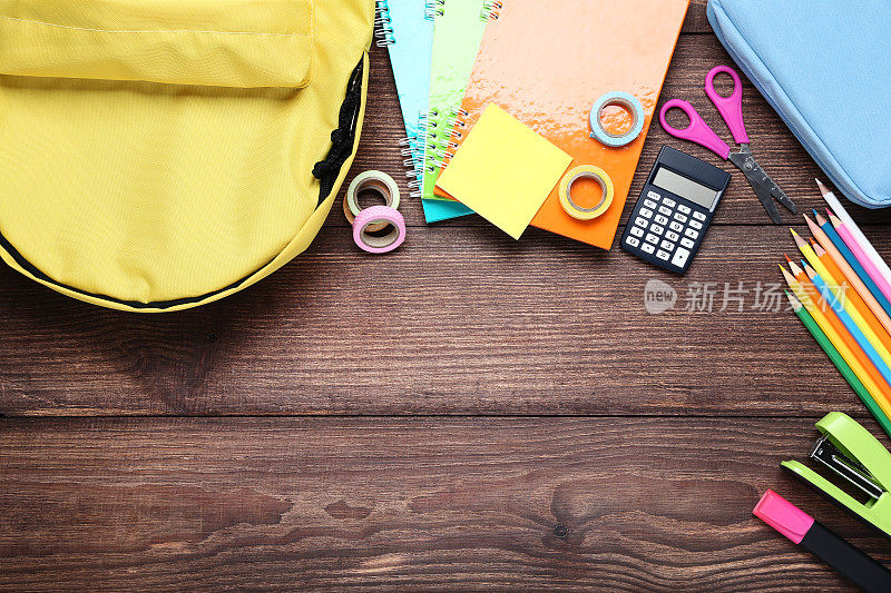 黄色的书包和学习用品放在棕色的木桌上