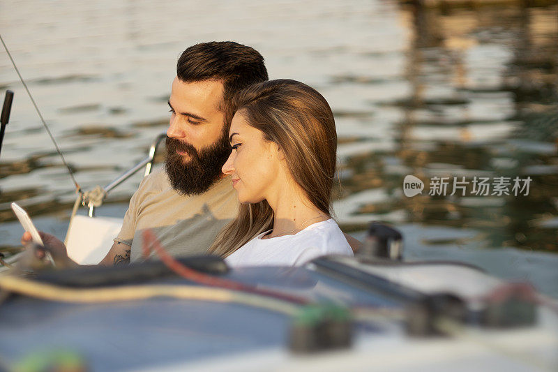 一对迷人的情侣在一艘帆船上放松、拍照和使用智能手机