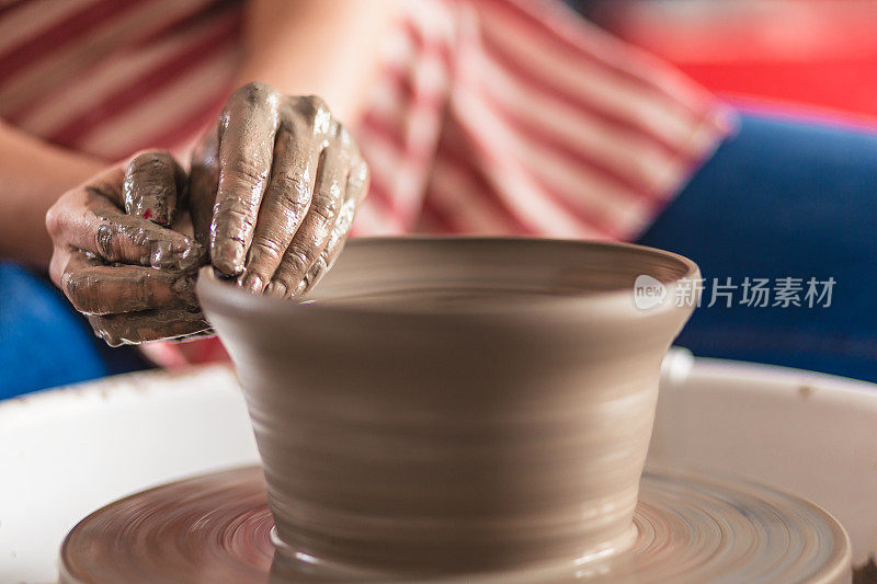 在艺术工作室里，女性的双手在陶轮上制作陶器