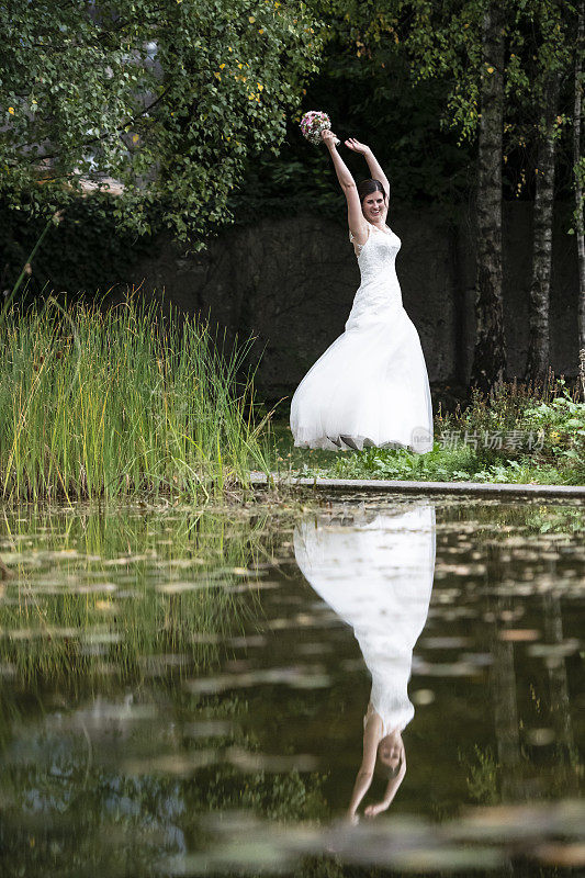 快乐的新娘举起双手在公园里蹦蹦跳跳