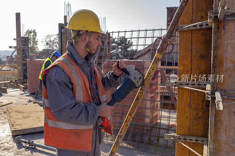 在一个阳光明媚的日子里，建筑工人正用金属磨床在建筑工地的屋顶上工作