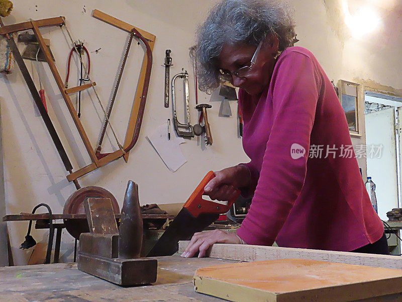 老妇人正在用手锯锯一块木板