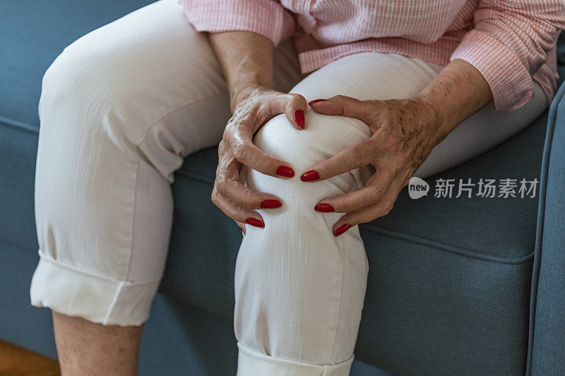 老妇人坐在沙发上忍受着腿部和膝盖的疼痛。