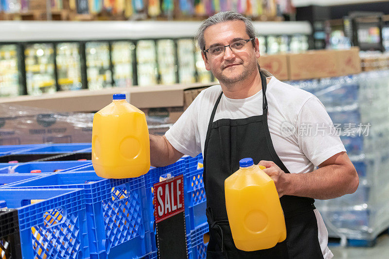 一个在超市工作的成年人手里拿着两加仑橙汁
