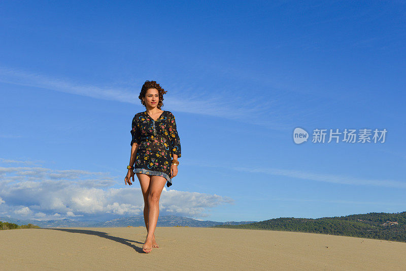 一个年轻漂亮的女人走在沙丘上。