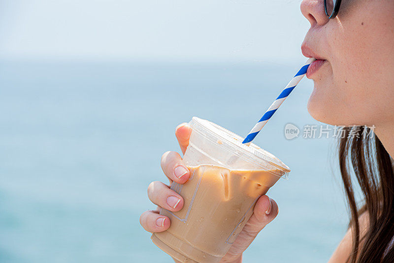 年轻女子在海滩喝冰咖啡的简介