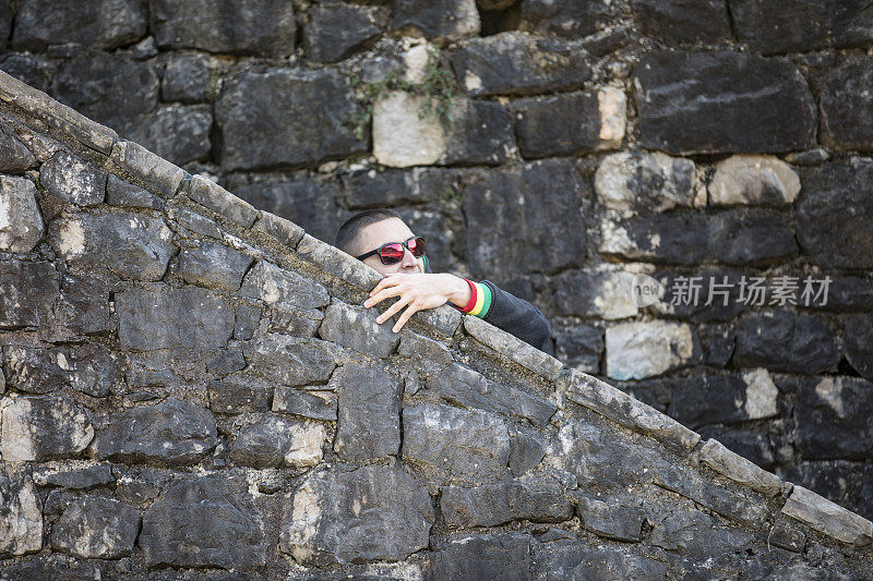 一名年轻的成年男子在一堵石墙外窥视